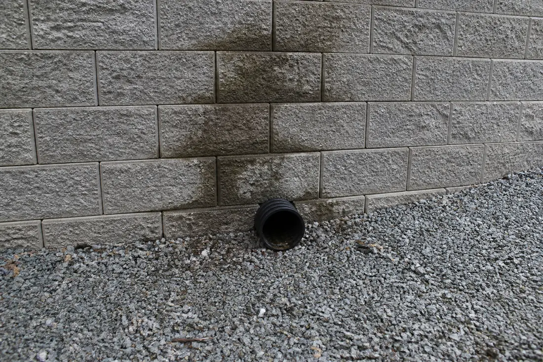 A perforated drain pipe outlet at the base of a retaining wall